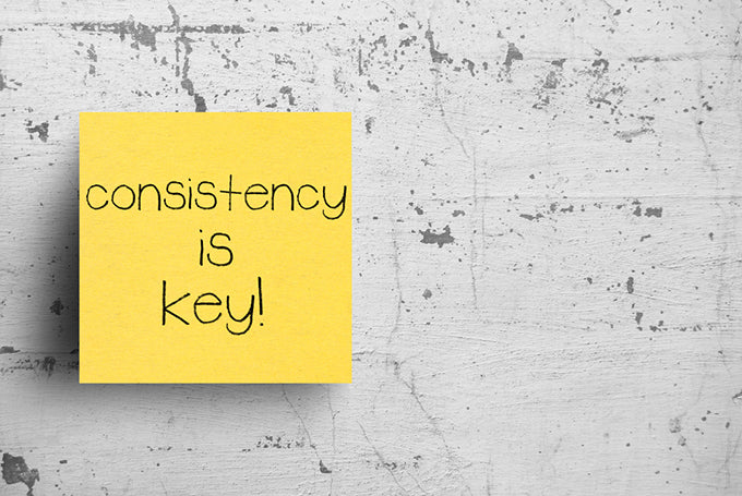 a sticky note on a concrete wall that says consistency is key