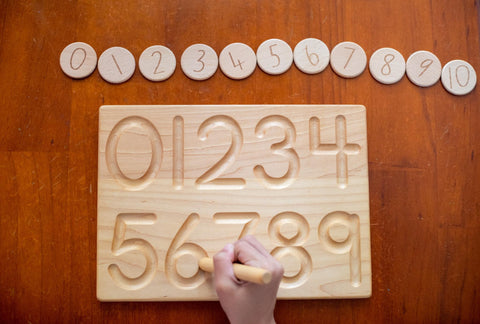 Numeral tracing using a wooden montessori board.