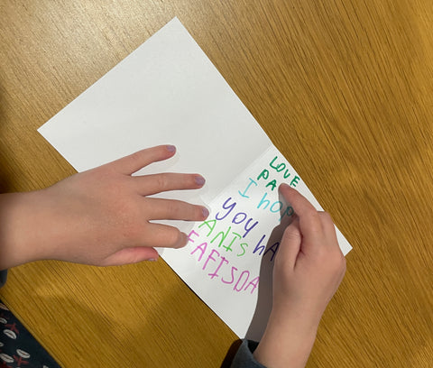 Young child writing on a birthday card.