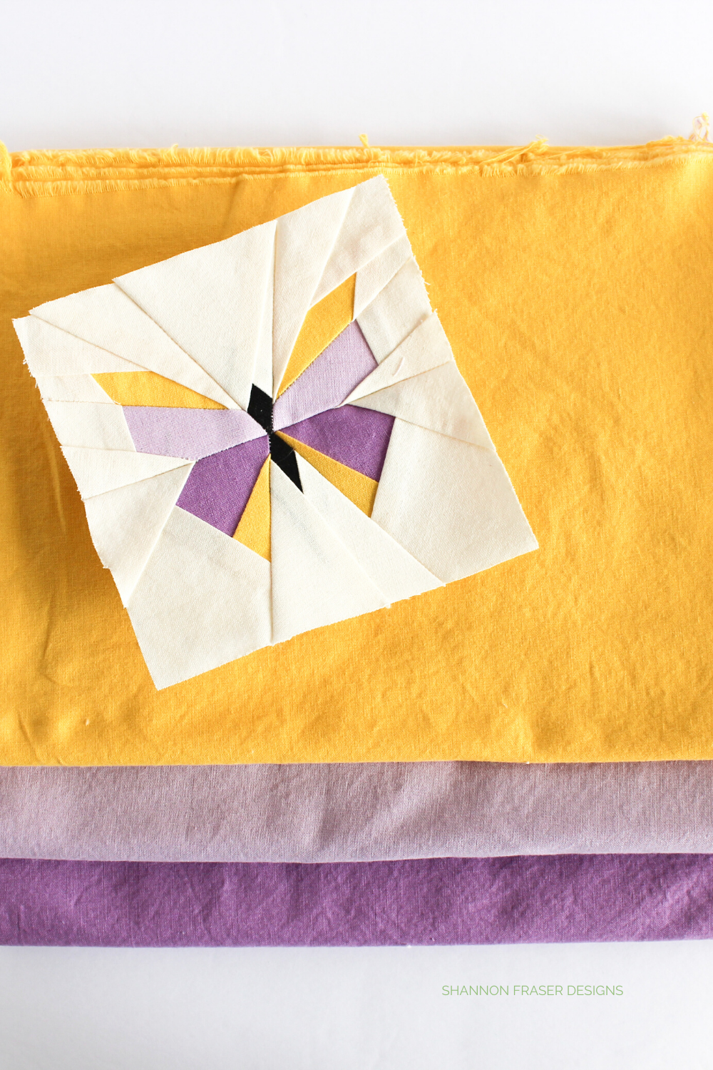 Paper pieced butterfly on top of a stack of fabric yellow, lavender and lilac