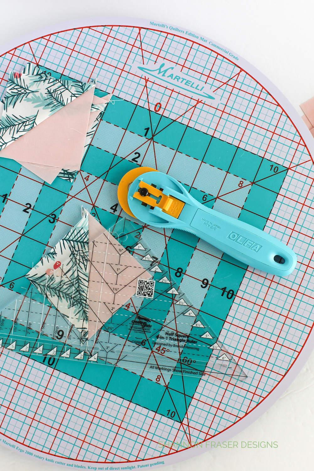 Half square triangle being trimmed on a Martelli round about mat with an Olfa splash rotary cutter and Creative Grids 4 in 1 triangle ruler | Shattered Star QAL Week 3: HSTs | Shannon Fraser Designs #quilting #quilttutorial