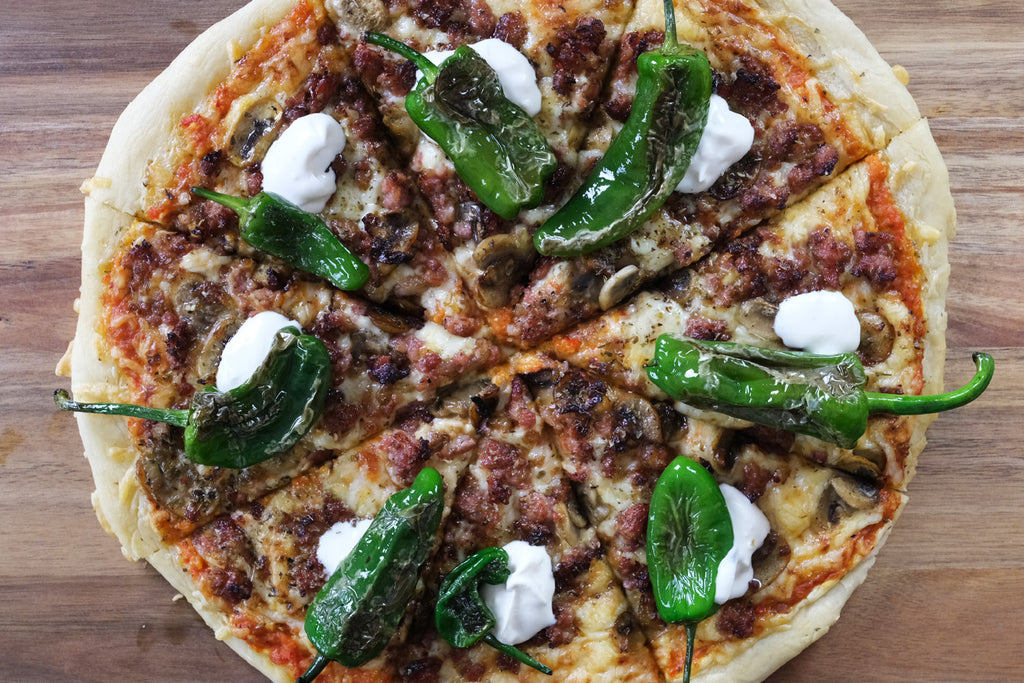 Pizza with Salsiccia, Ajvar Relish and Pimientos de Padron on a wooden cutting board