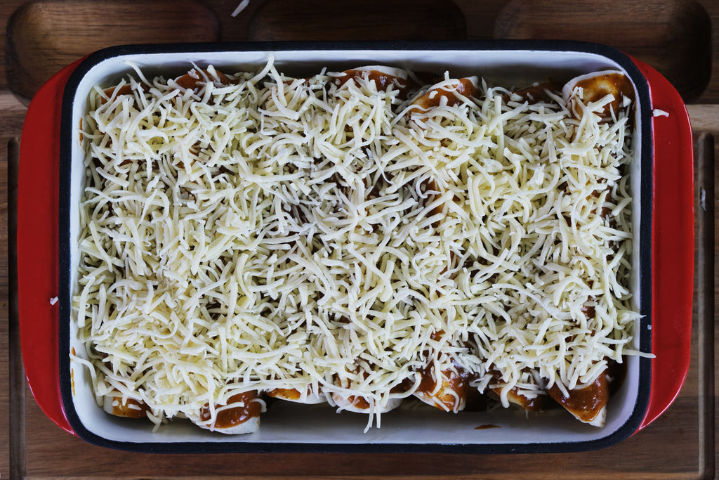 enchiladas topped with cheese in an enameled cast iron roasting pan