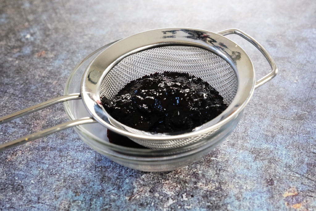 pressing mashed blueberries through a sieve