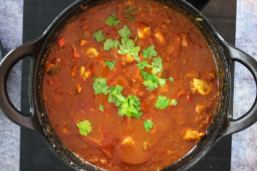 balti chicken curry in a cast iron balti dish topped by coriander