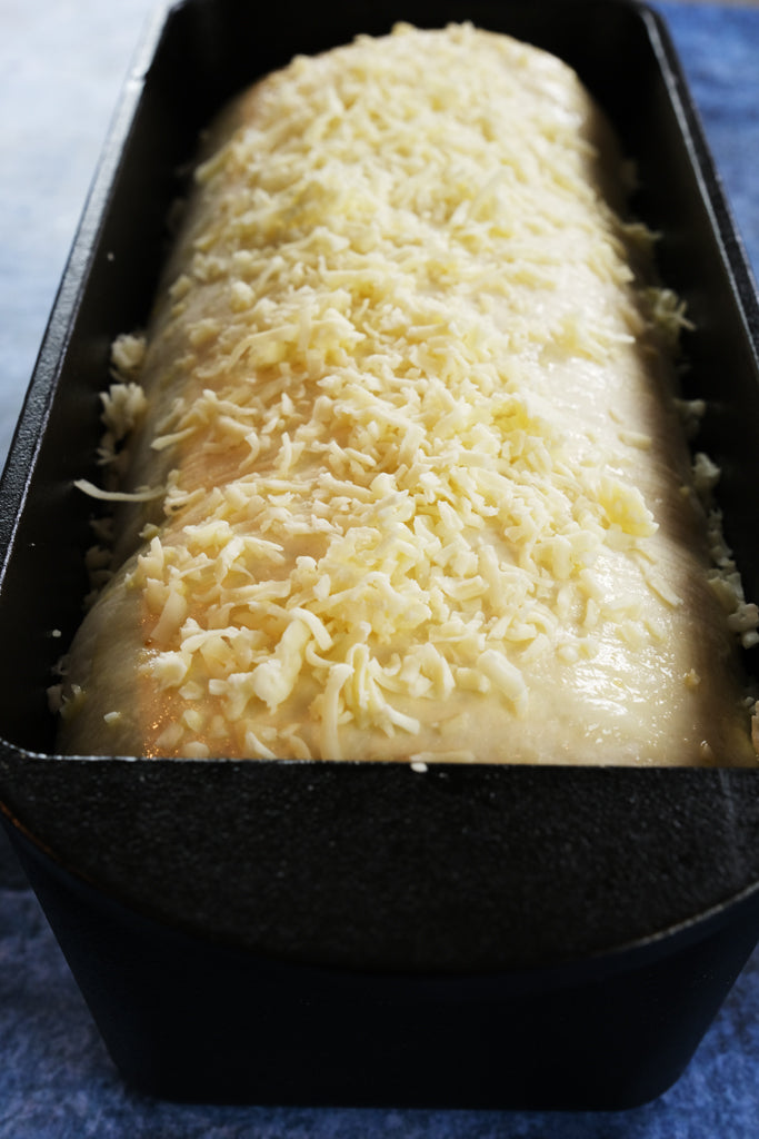 pesto bread with cheese on top in a cast iron bread pan