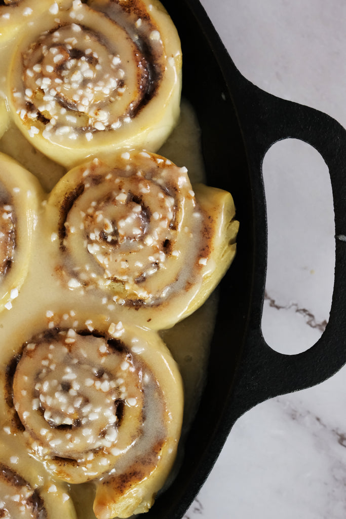 cinnamon rolls in a cast iron pizza baking pan topped with icing glaze