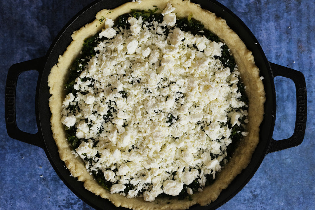 spinach topped with feta cheese in a cast iron skillet with loop handles