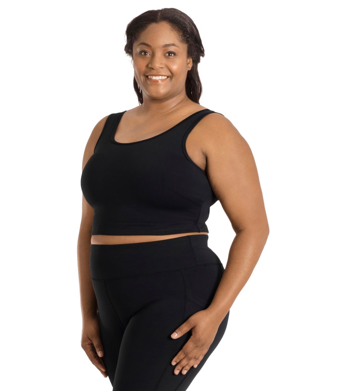 Plus size woman, angled to the left back, wearing JunoActive plus size JunoStretch Scoop Bra in black. The woman is wearing black plus size JunoActive leggings. Her arms fall naturally to her side with her hands on her thighs.
