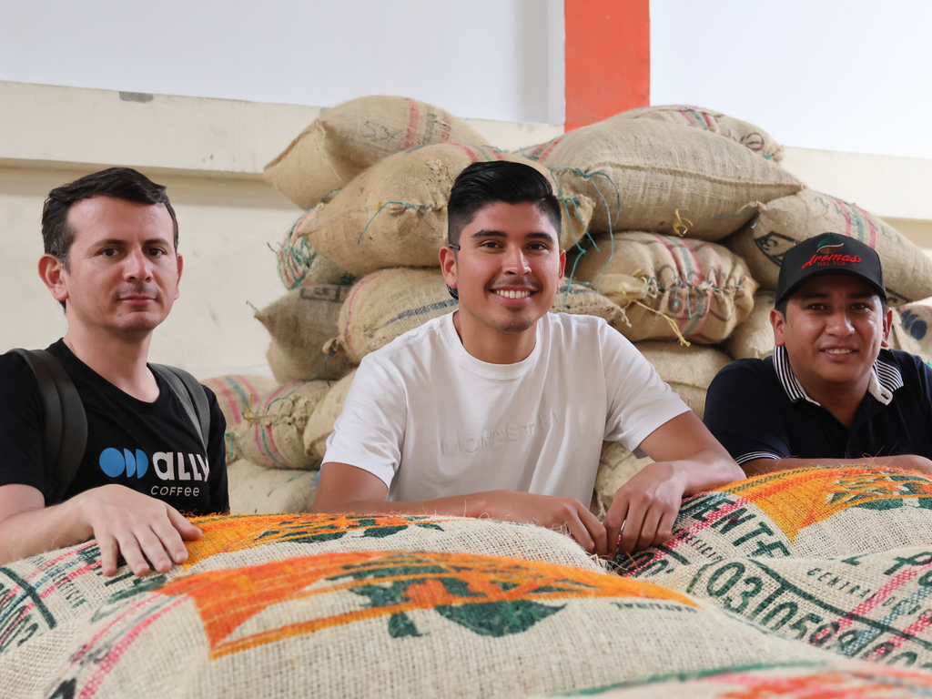 Three people standing for a photo with burlap coffee bags in front of and behind them