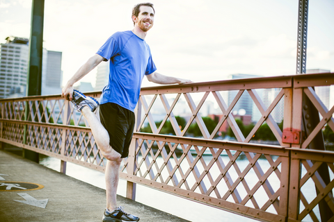 Man in a blue t-shirt and black shorts on a bridge performing a quad stretch