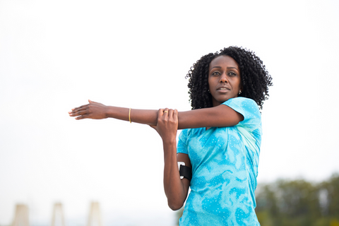 dark skinned, curly haired woman in turquoise shirt doing a shoulder stretch with her arm across her body