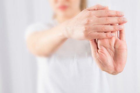 hands in the foreground performing a wrist stretch, background is woman's torso in a white t-shirt