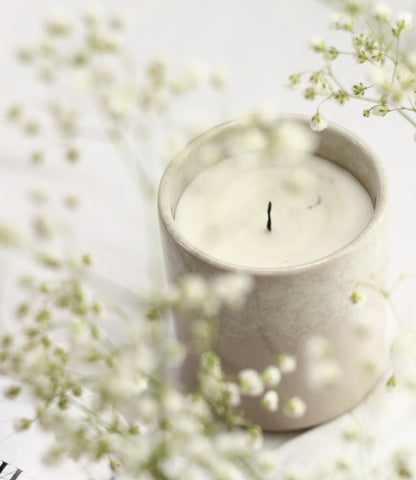 Candle in a stone holder with white and green wildflowers at the forefront