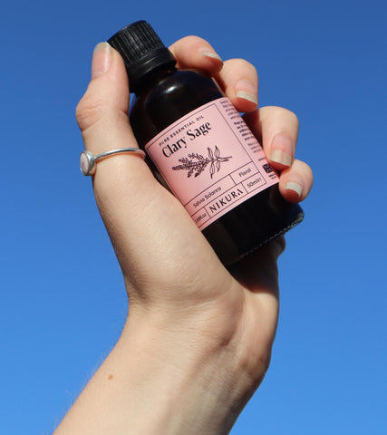 Hand holding up a clary sage 50ml against a bright blue sky