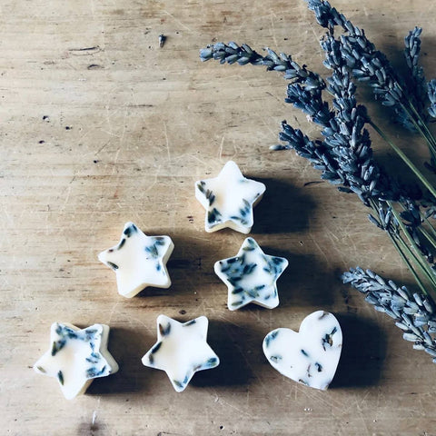 Five star shaped wax melts and one heart shaped. All with dried lavender inside next to a bunch of dried lavender sprigs