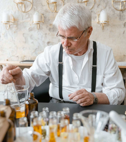 Man with white hair, white shirt and suspenders mixing perfume in a beaker