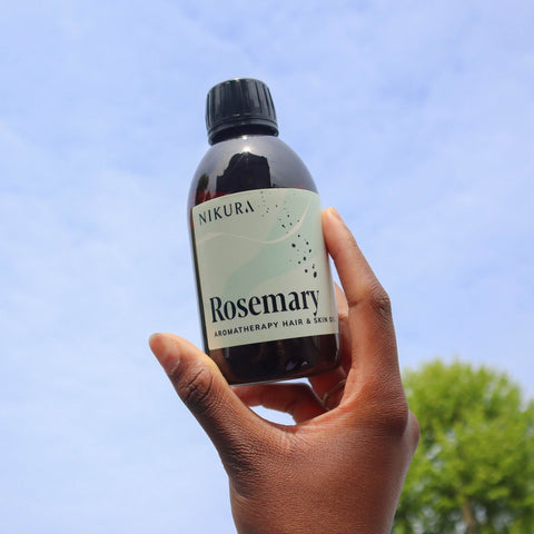 Hand holding up our rosemary oil for hair 250ml against a blue sky background