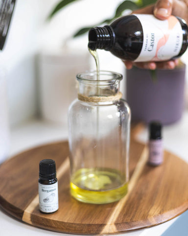 250ml bottle of castor oil being poured into a glass jar with a 10ml bergamot oil bottle next to it