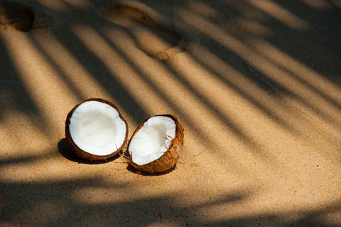 Halved coconut on some sand with shadows of the leaves over