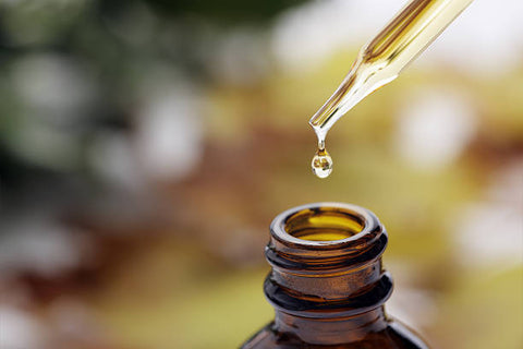 Close up of the neck of an essential oil bottle with the dropper dropping oil into the bottle