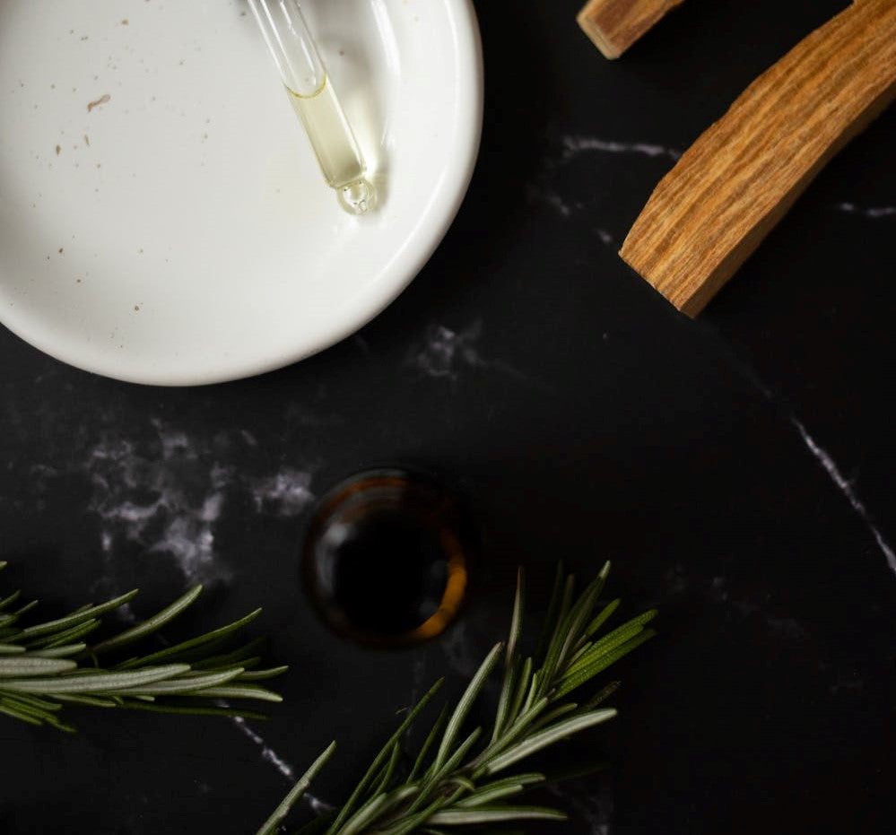 Rosemary sprigs, bottle and essential oil dropper on black background