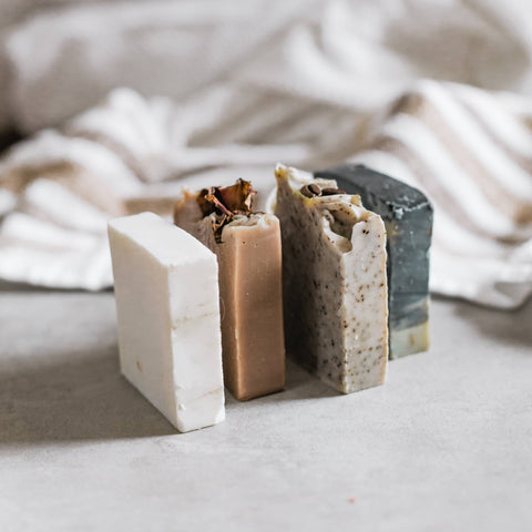 Four hand made soap bars stood up in a row with a cream blanket as the background
