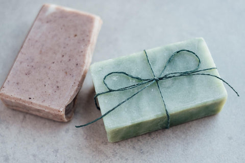 Two soap bars next to each other one pink and one green with a green bow made out of string