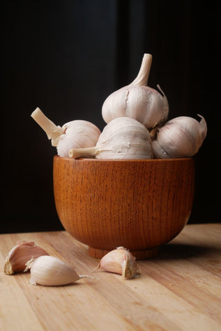 few bulbs of garlic in a wooden bowl with cloves of garlic at the base