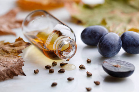 Grapeseed oil vial on its side with grapes and grapeseeds around it