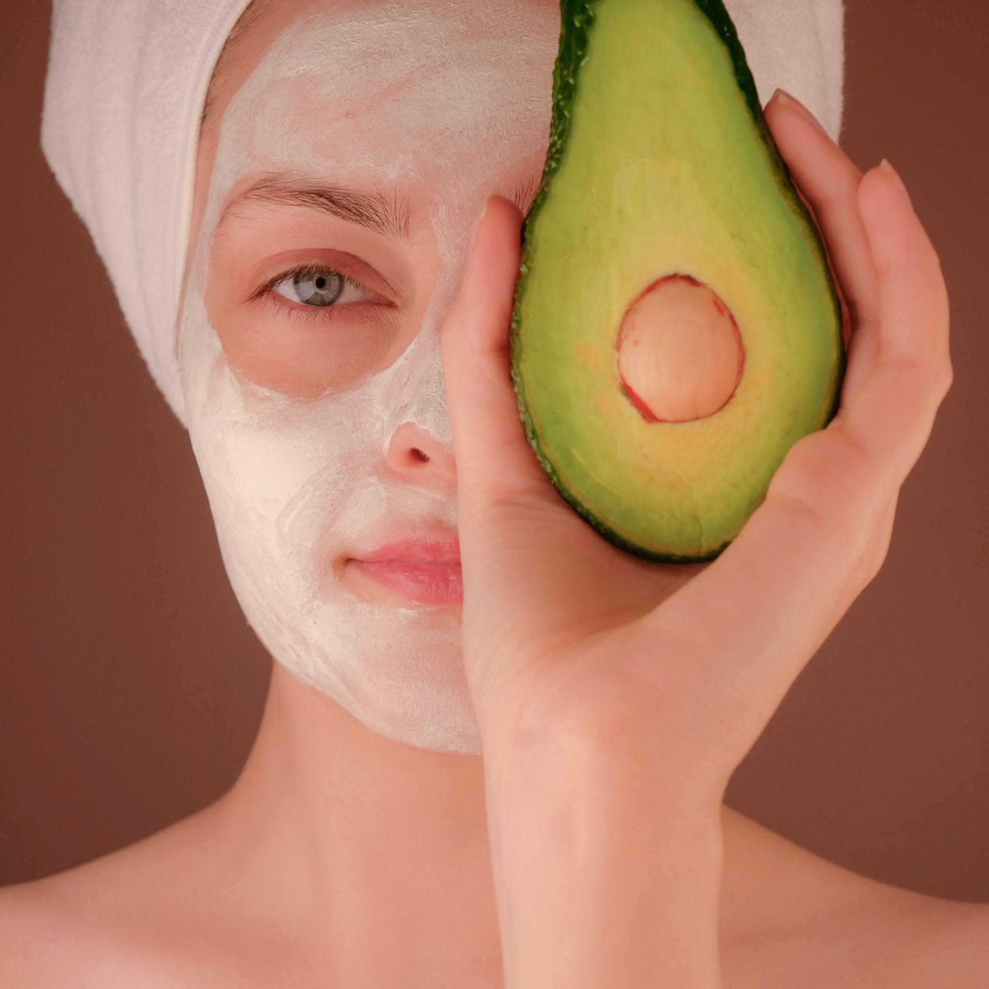 Woman holding half an avocado in front of her eye.