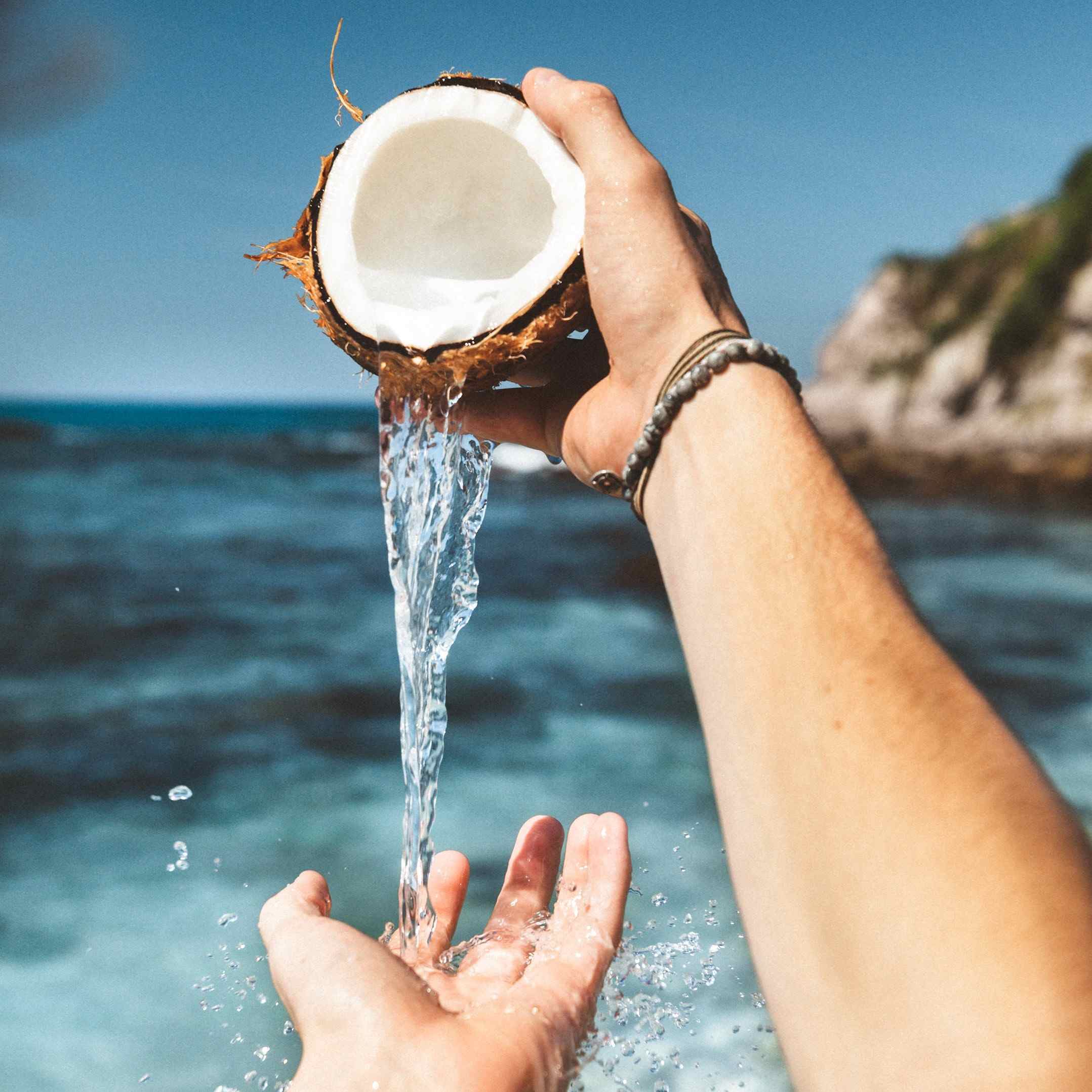 Coconut shell spilling water onto a person's hand.