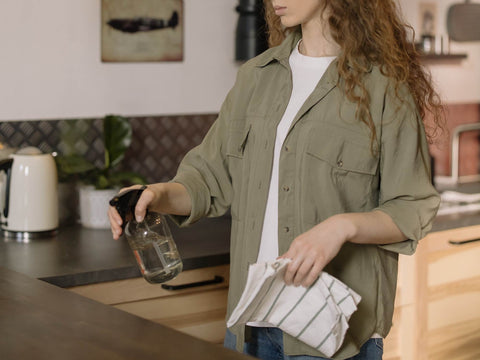 Woman holding a spray bottle ready to spray it onto a kitchen surface with a cloth in hand