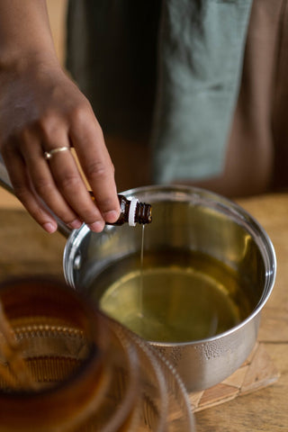 Person pouring fragrance oil into a pan of melted wax