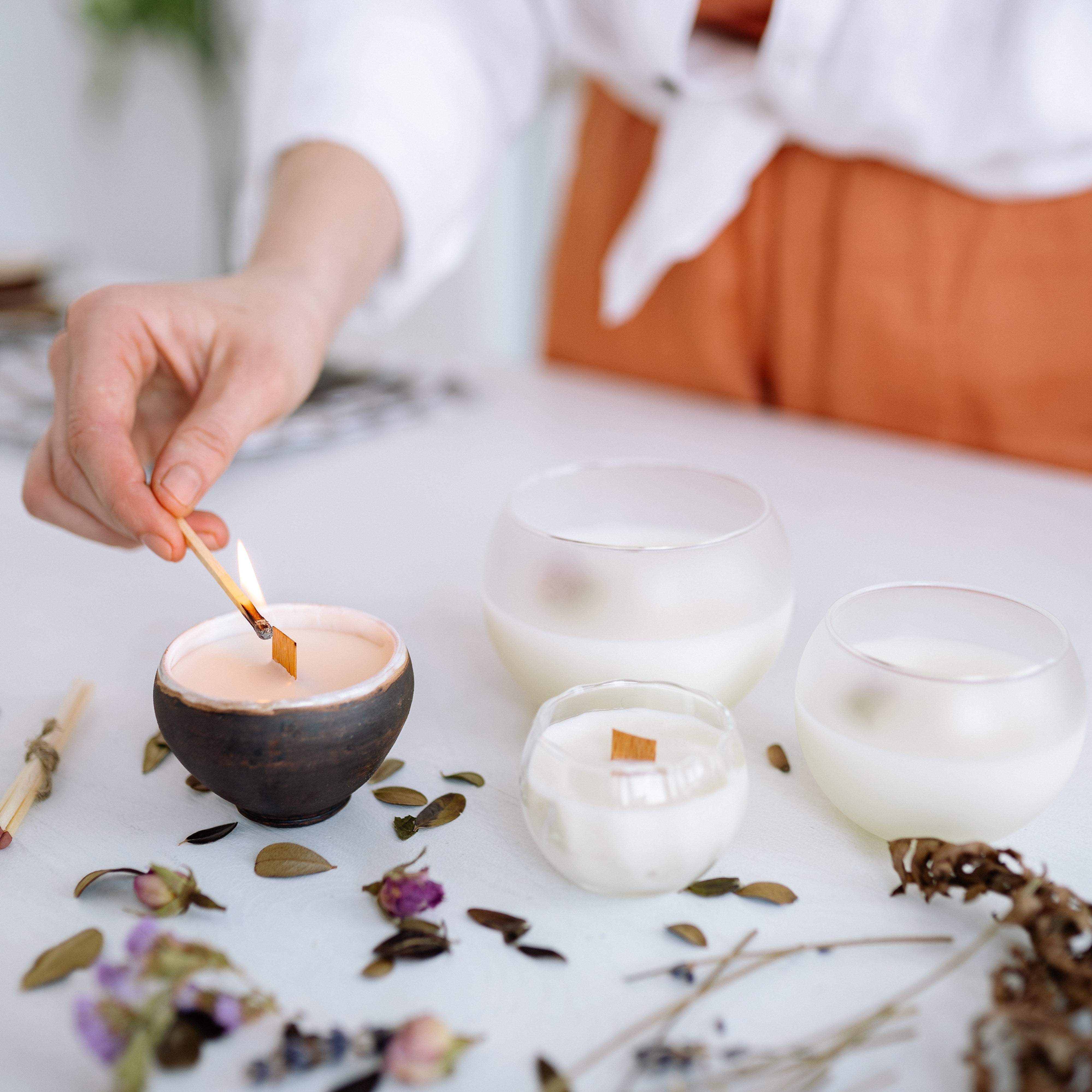 Women lights a candle on a table, with other candles and petals on the surface