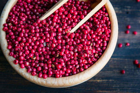 A wooden bowl of pink peppercorns