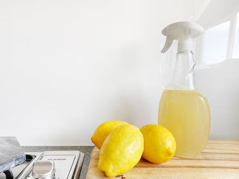 Cleaning spray placed onto a kitchen side next to a sink with three lemons at the base of the spray bottle