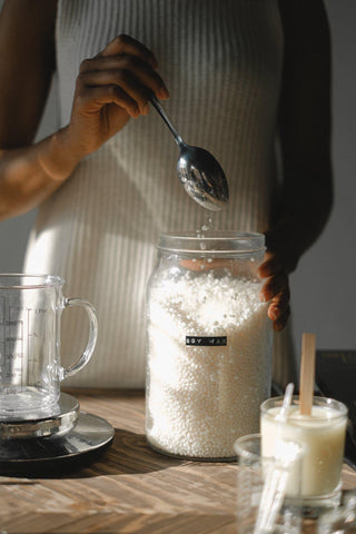 woman holding a spoon ready to decant soy wax from a large jar of it