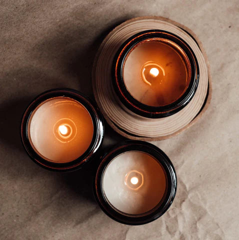 three lit candles in amber glass jars with wooden background