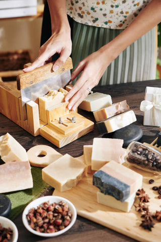 Various soap making equipment with ready soap bars. Woman is cutting soap using a wooden slicer