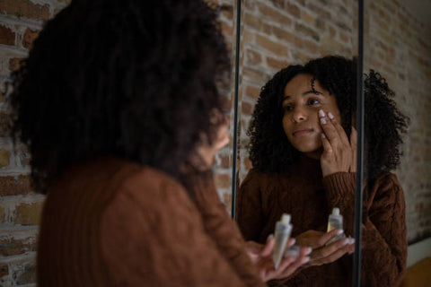 Woman looking at herself in the mirror applying cream to her cheek