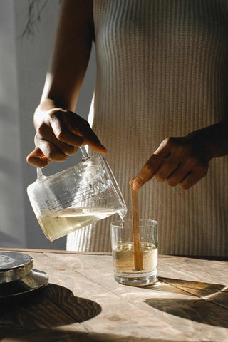 Woman pouring wax into a clear candle jar with a wooden wick