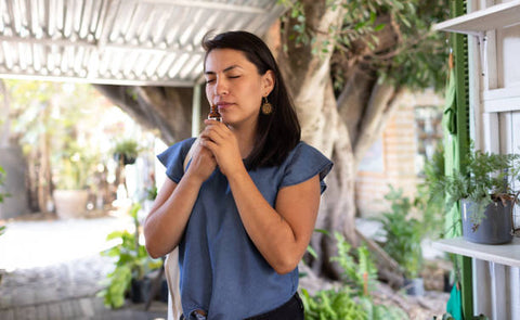 Woman holding an essential oil bottle and smelling it. The woman is stood outside