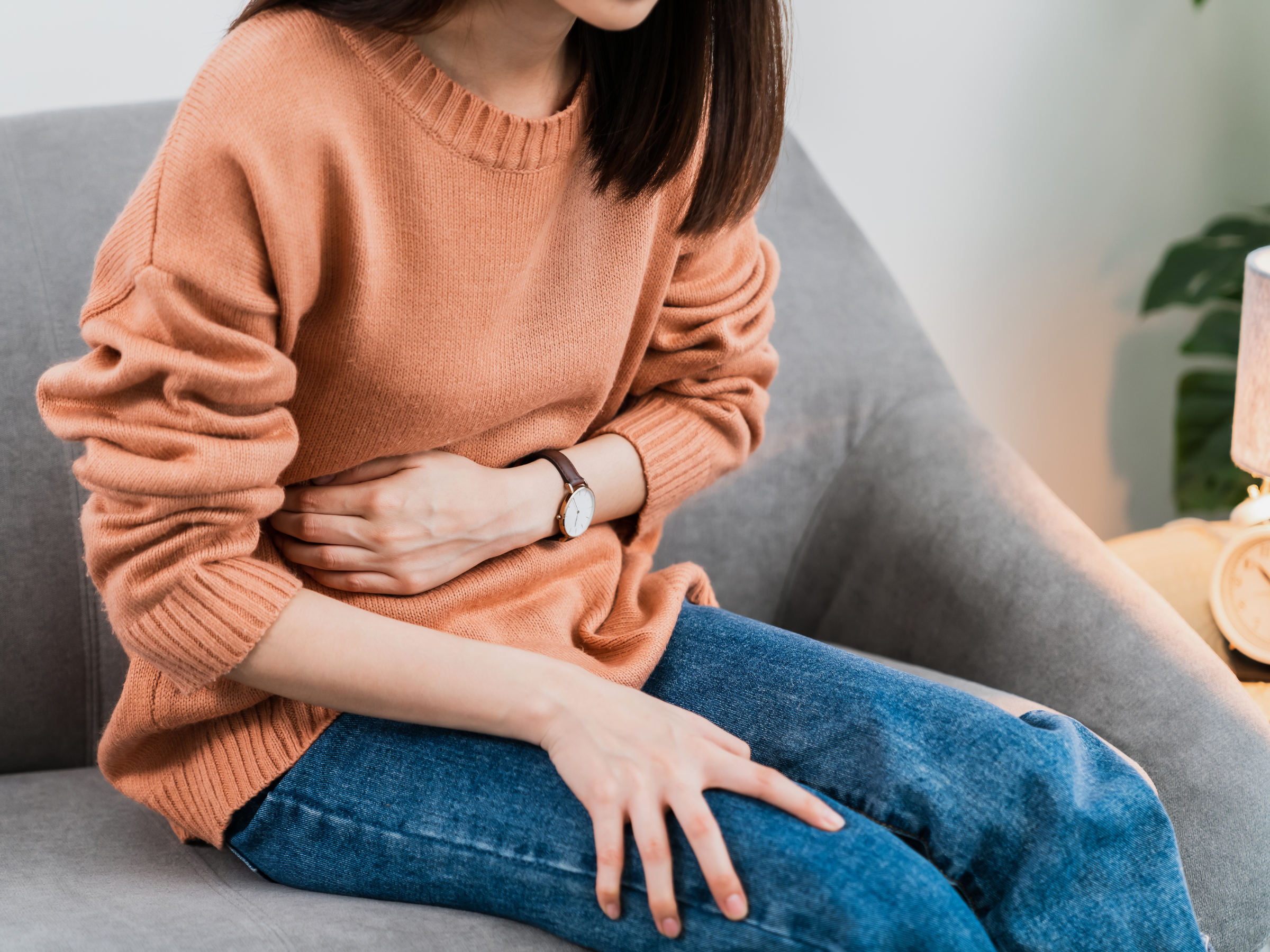 Woman in tan sweater and blue jeans clutching her stomach