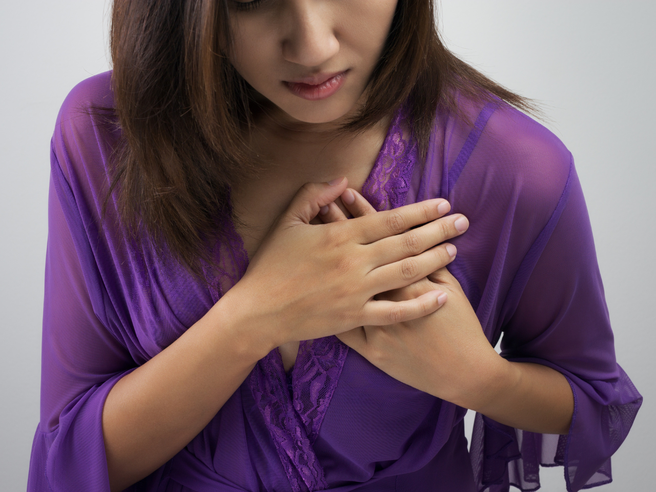 Woman dressed in purple shirt clutching chest due to chest pain
