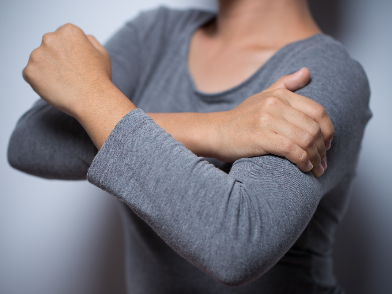 Woman clutching arm due to arm pain, a symptom of heart attack.