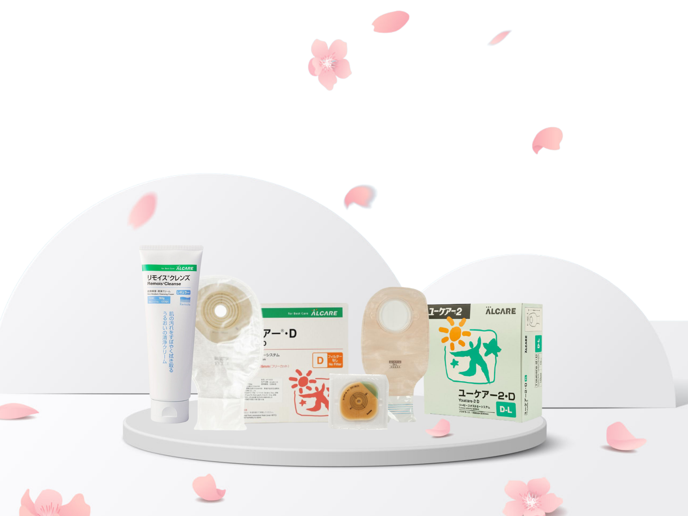 ALCARE free stoma starter kit displayed on a white table, with sakura flower petals falling on the products. Product from left: Remois Cleanse cleansing cream, Youcare D stoma bag, Youcare 2F faceplate, Youcare 2D stoma bag.