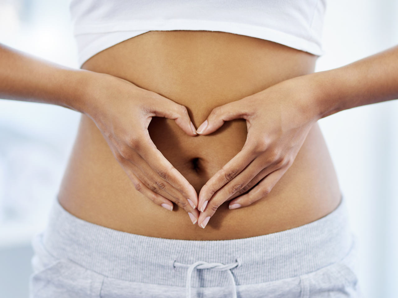 Lady in white outfit posing with a heart shaped hand at the center of her stomach to illustrate a healthy gut