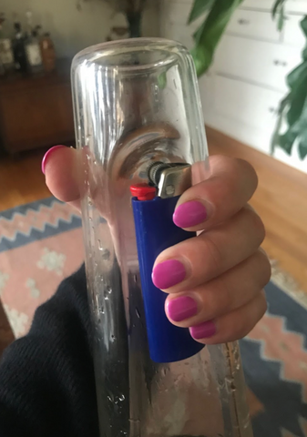 A hand is holding the lighter into the indent of the bong.