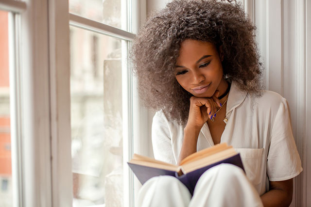 woman reading book in window